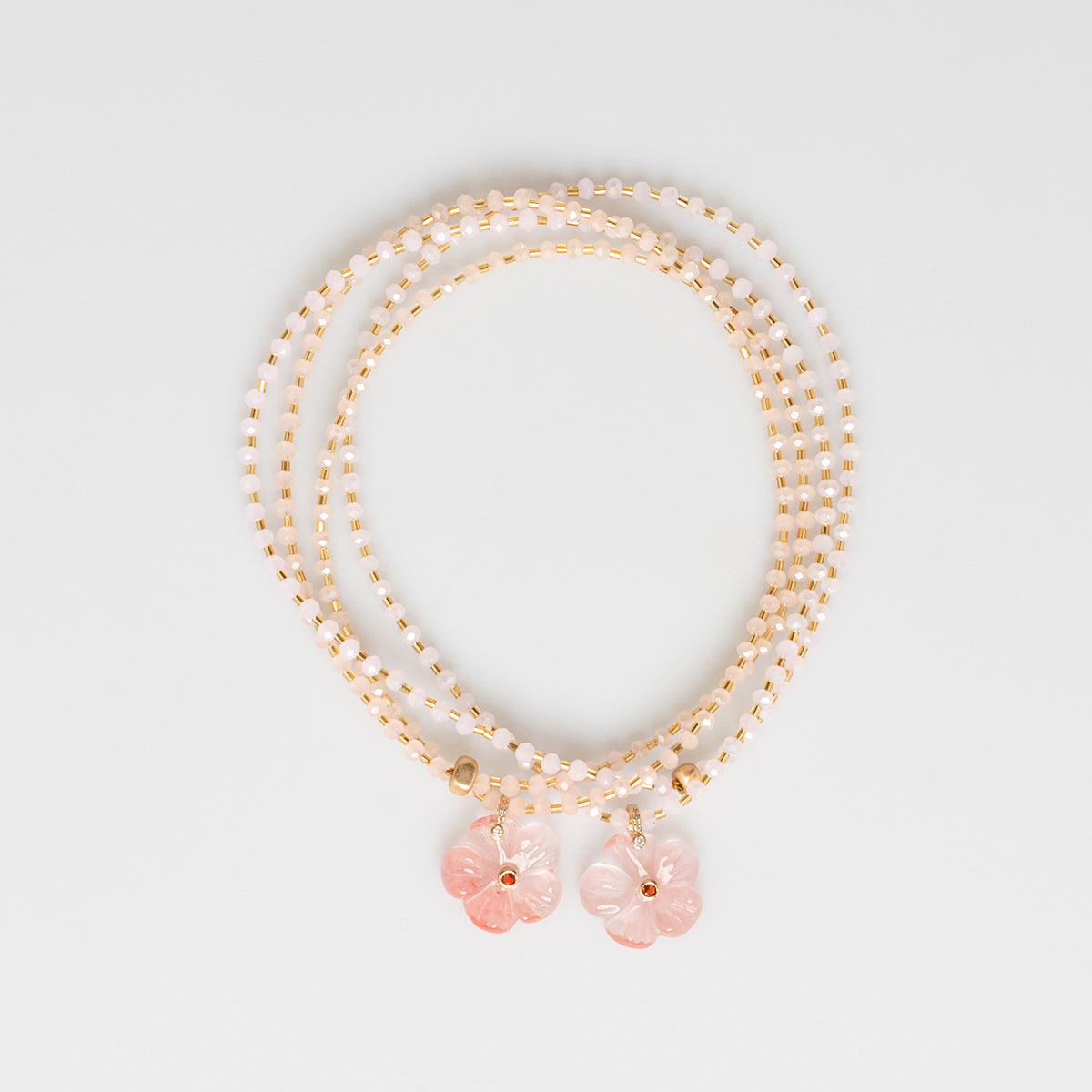 A multi-strand beaded necklace with rose gold-toned beads and two dangling pink flower charms, displayed on a clean light gray background.